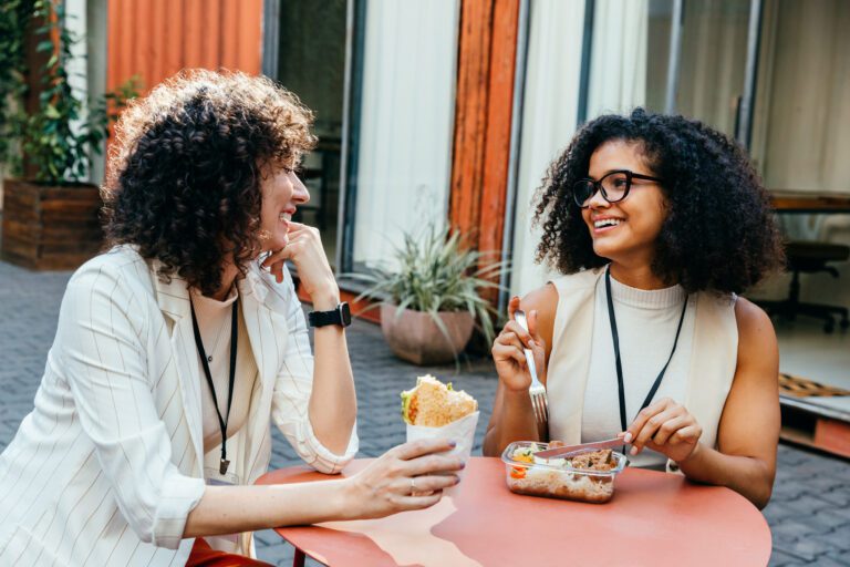 two women sharing a lunch at an outdoor circular table.