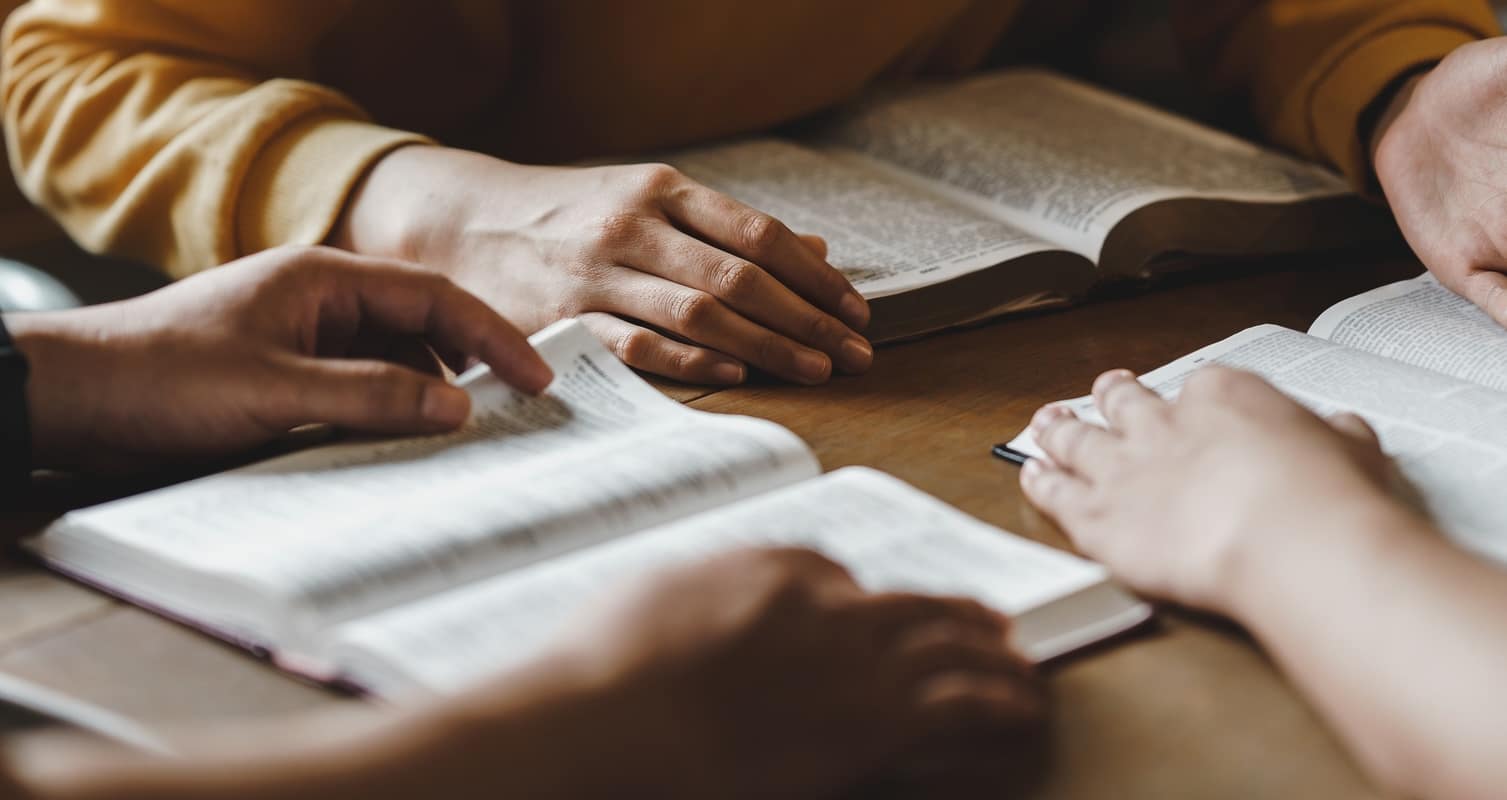 Group of people reading open Bibles on a wooden table during a study session.